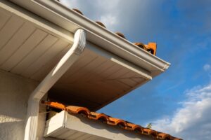 House corner with white planks siding and roof with steel gutter rain system and pipes installation